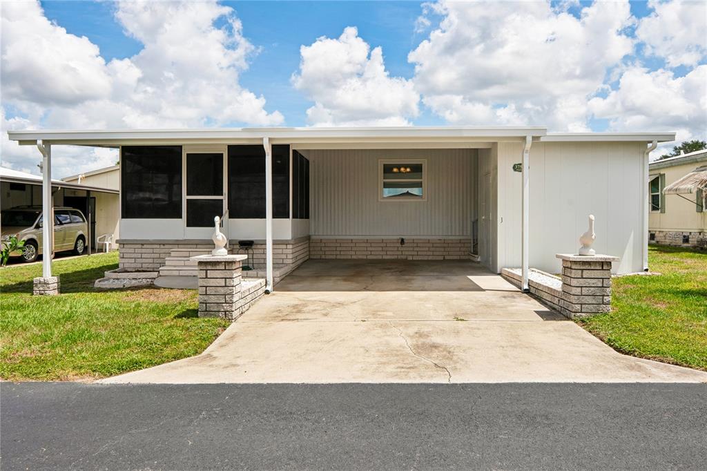 A single-story manufactured home features a screened porch, a concrete carport, and two decorative statues — 37537 PINATA AVENUE, ZEPHYRHILLS, FL