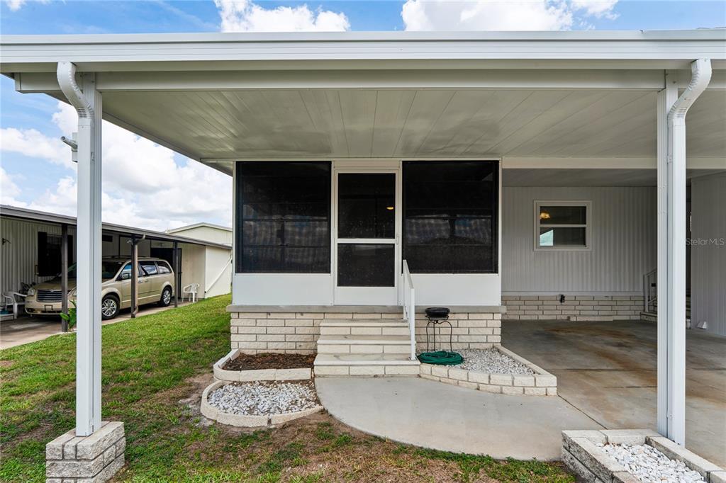 A screened-in porch with concrete steps sits under a covered carport area — 37537 PINATA AVENUE, ZEPHYRHILLS, FL