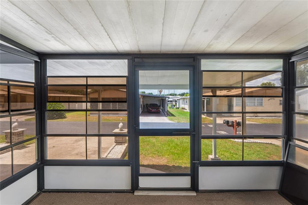 A screened-in porch with large windows looking out onto a residential street and carport — 37537 PINATA AVENUE, ZEPHYRHILLS, FL