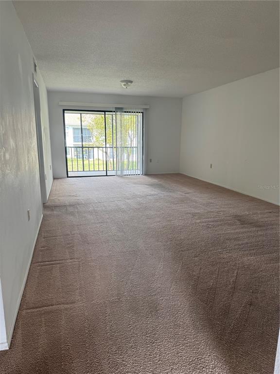 An empty living room features beige wall-to-wall carpeting, white walls, and a sliding glass door — 106 LAKESIDE COURT, OLDSMAR, FL