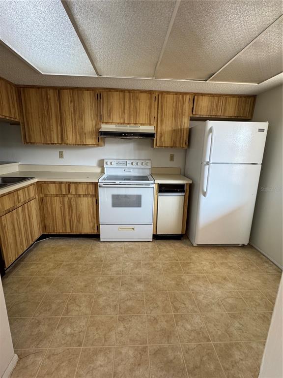 A kitchen features wood-grain cabinets, white appliances, a drop ceiling, and light-colored tile flooring — 106 LAKESIDE COURT, OLDSMAR, FL