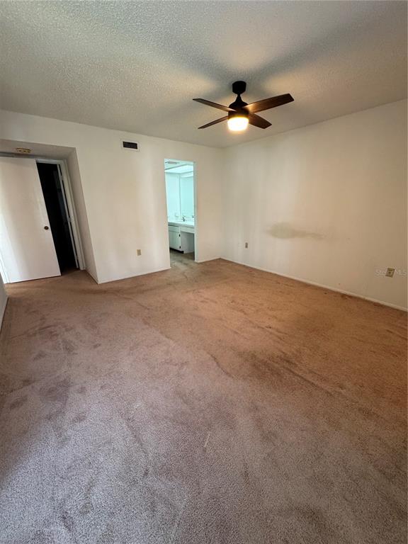 An empty bedroom with beige carpet, a ceiling fan, and an attached bathroom doorway — 106 LAKESIDE COURT, OLDSMAR, FL