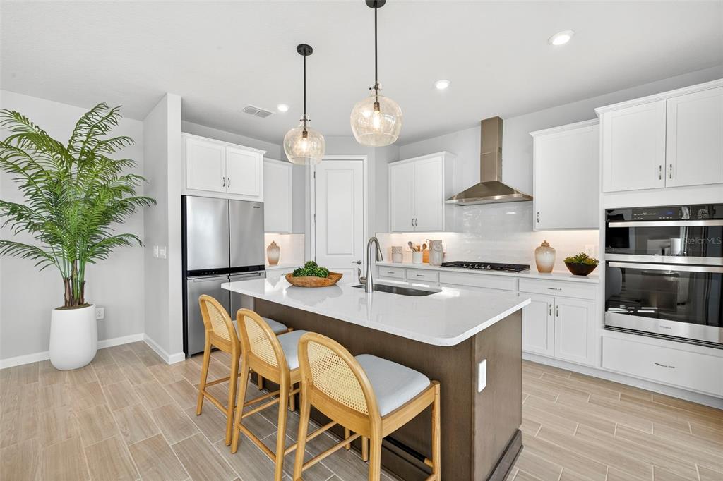 A modern kitchen features white cabinetry, a dark wood island with bar stools, and stainless appliances — 34877 ARBOR RETREAT DRIVE, DADE CITY, FL