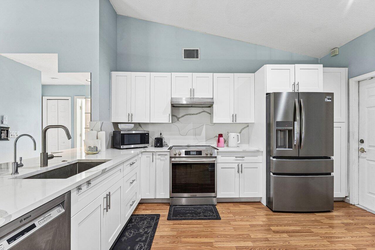 A kitchen features white cabinets, stainless steel appliances, marble-look countertops, and wood-style flooring — 13564 N 63rd Ln Lane N, FL 33412, FL