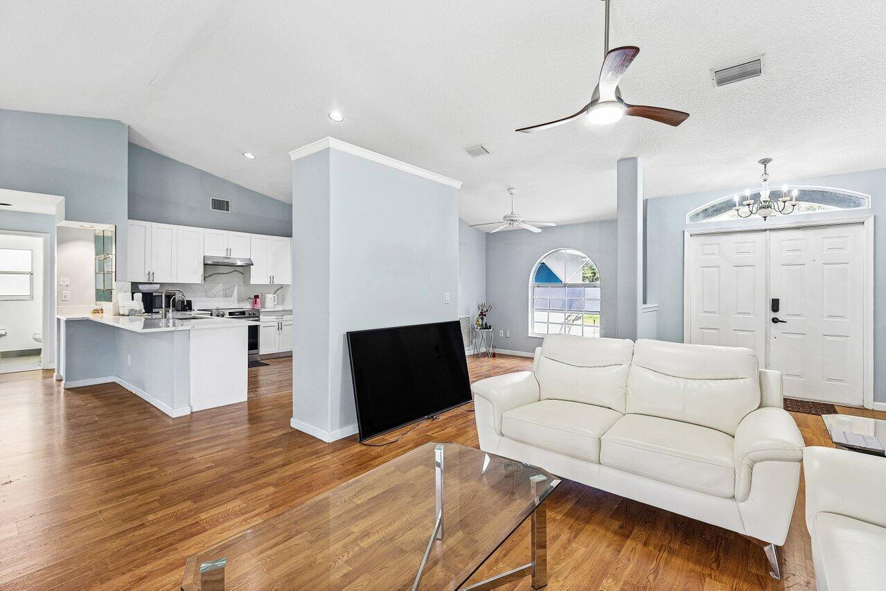 A living room with wood floors, a white sofa, and an open kitchen with white cabinets — 13564 N 63rd Ln Lane N, FL 33412, FL