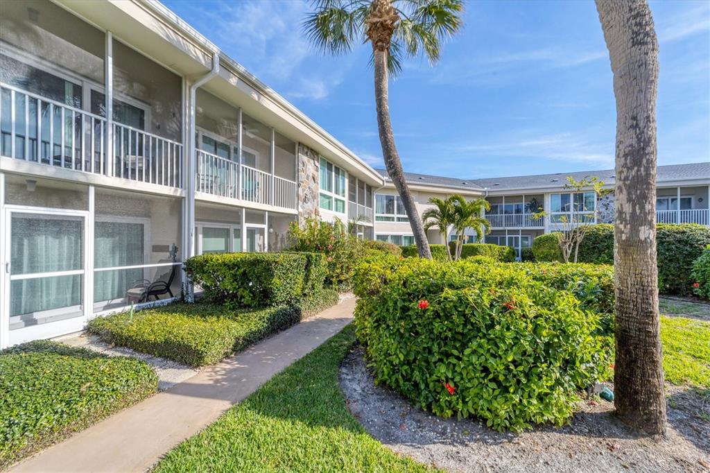 A two-story apartment building with screened balconies, a paved walkway, and manicured landscaping — 500 S WASHINGTON DRIVE UNIT 18B, SARASOTA, FL