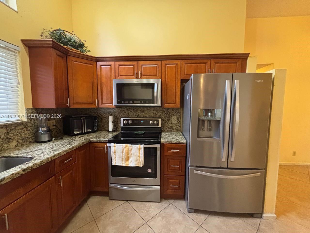 A kitchen features wood cabinets, granite countertops, stainless steel appliances, and tile flooring — 7390 S Pinewalk Dr S, Margate FL 33063, MARGATE, FL