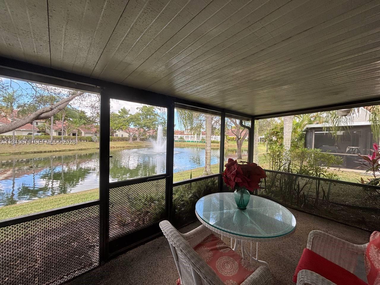 A screened-in patio features a glass-topped table and views of a pond with a fountain — 7390 S Pinewalk Dr S, Margate FL 33063, MARGATE, FL
