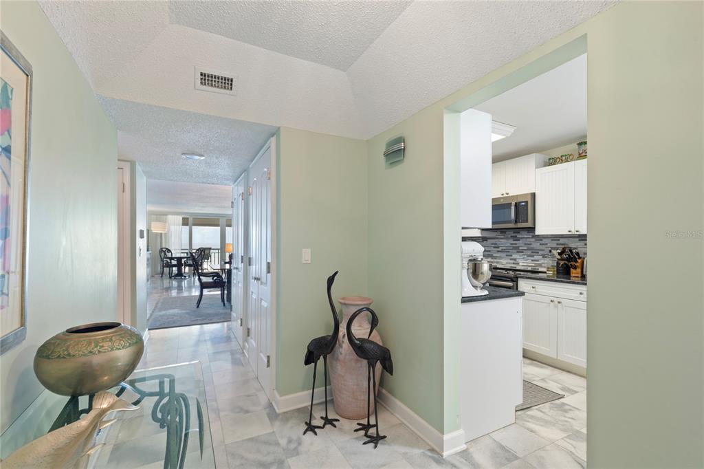A hallway with marble floors leads to a kitchen and a living area with balcony views — 2900 GULF BOULEVARD UNIT 201, BELLEAIR BEACH, FL