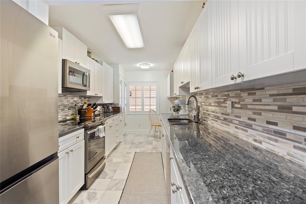 A galley kitchen features white cabinets, dark granite countertops, stainless steel appliances, and tile flooring — 2900 GULF BOULEVARD UNIT 201, BELLEAIR BEACH, FL