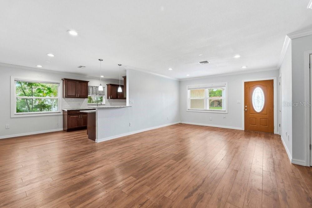 An open-concept living room features light gray walls, wood-look flooring, and an adjacent kitchen area — 1920 64TH AVENUE N, ST PETERSBURG, FL