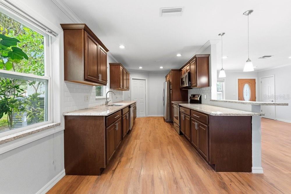 A kitchen features dark wood cabinets, granite countertops, stainless steel appliances, and light wood flooring — 1920 64TH AVENUE N, ST PETERSBURG, FL