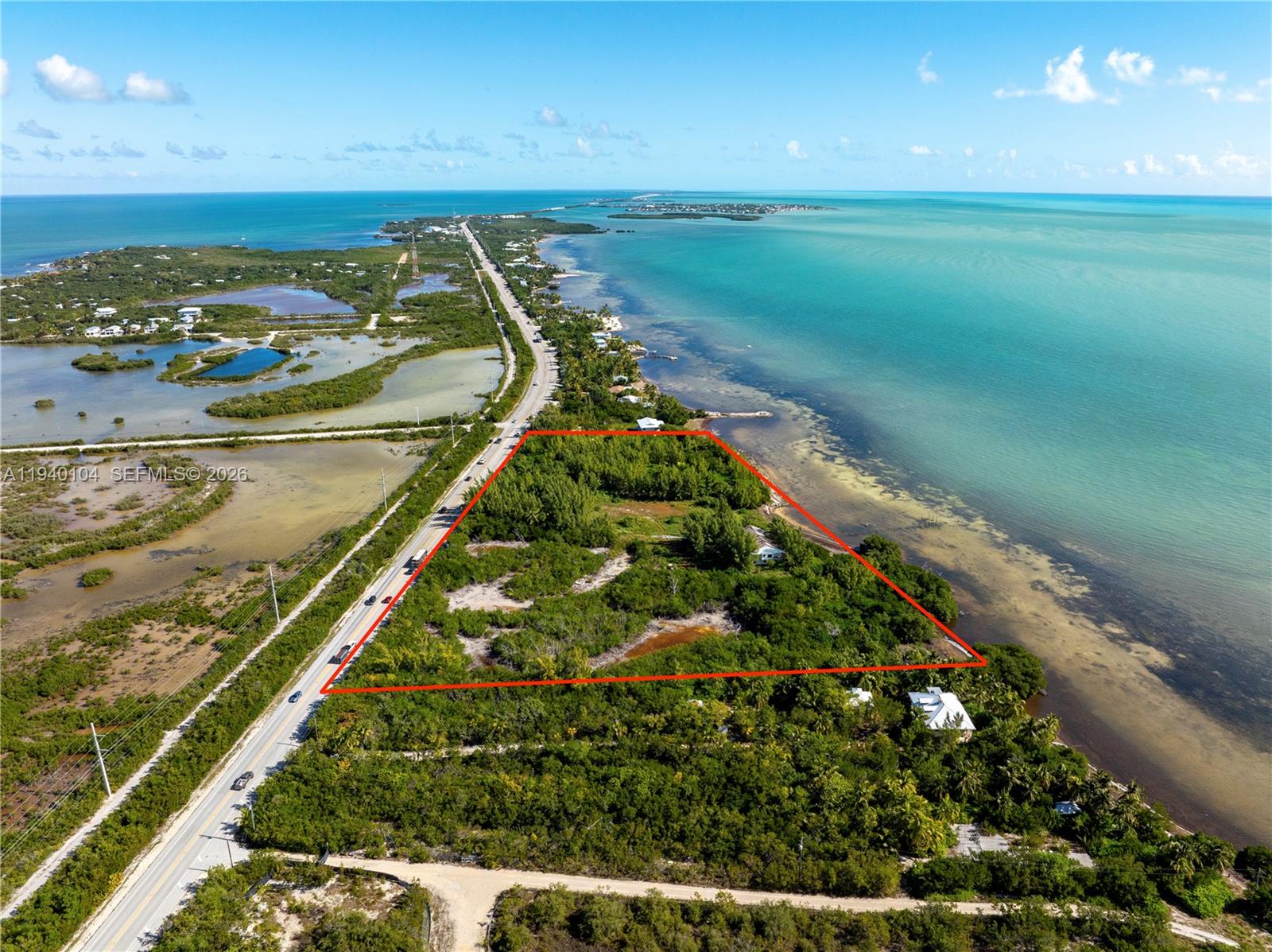 An aerial view shows a vacant, vegetated waterfront lot outlined in red along a highway — 57478 Overseas Hwy, Marathon FL 33050, MARATHON, FL