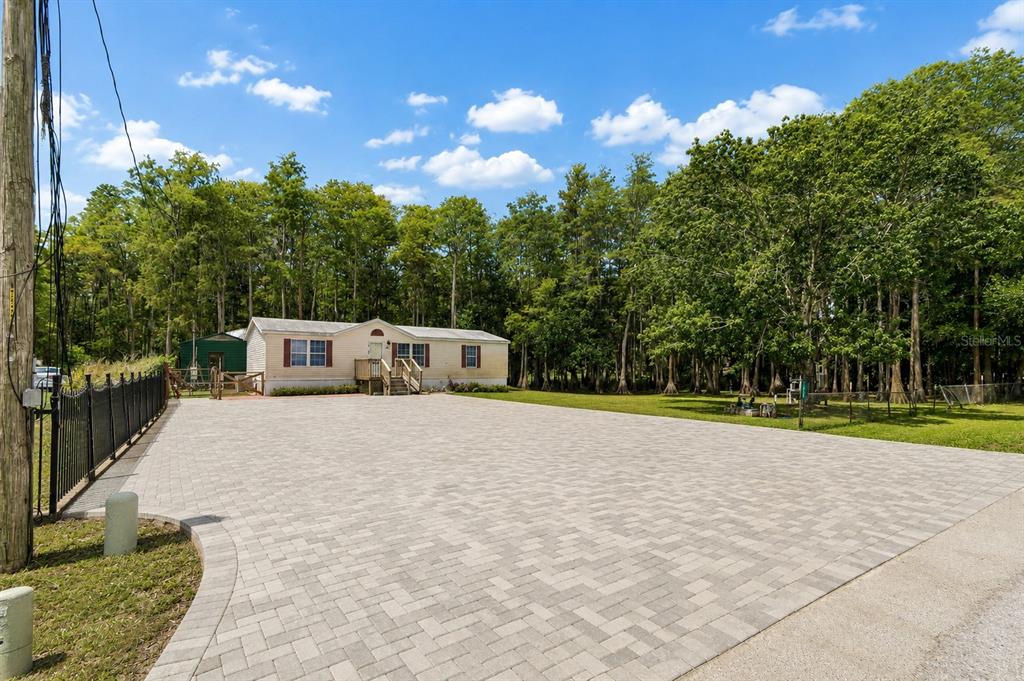 A single-story house sits behind a large paved driveway surrounded by trees — 17808 DOGWOOD DRIVE, LUTZ, FL