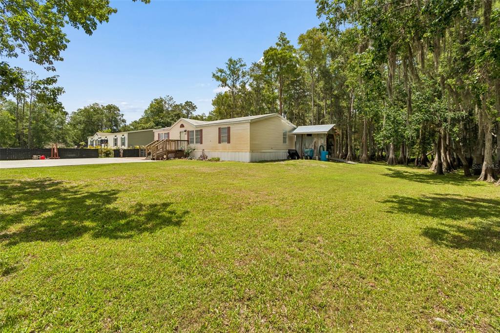 A single-story mobile home sits on a large grassy lot bordered by mature trees — 17808 DOGWOOD DRIVE, LUTZ, FL