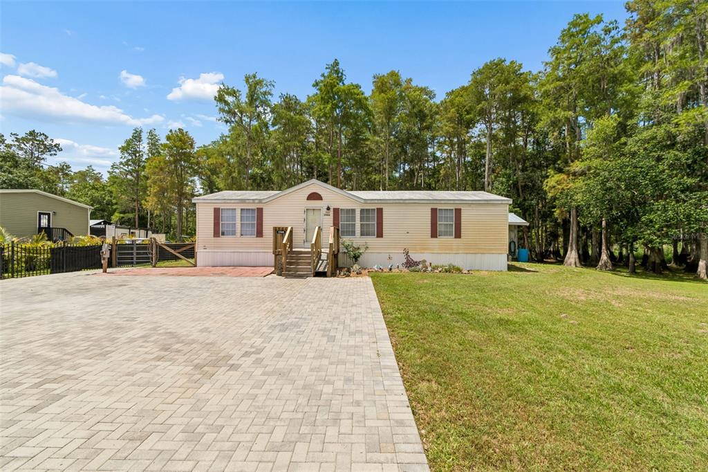 A single-story manufactured home with a paved driveway sits on a grassy lot near trees — 17808 DOGWOOD DRIVE, LUTZ, FL