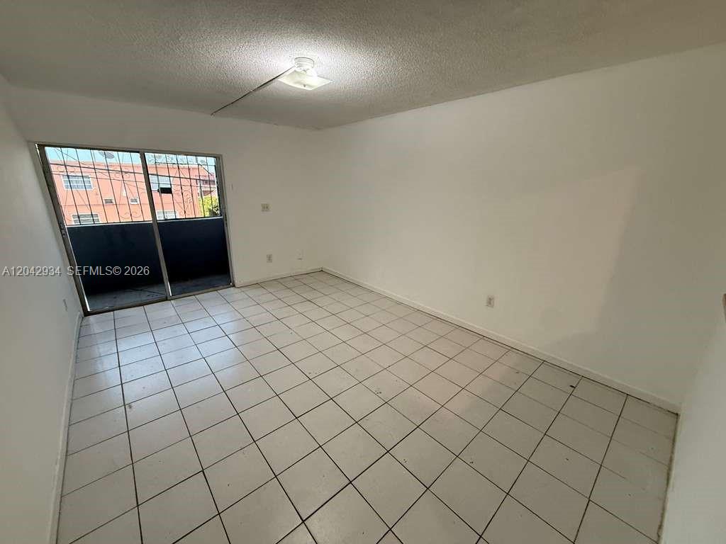 An empty room features white walls, light-colored tile flooring, and a sliding glass balcony door — 4370 NW 11th St # 214, Miami FL 33126, MIAMI, FL