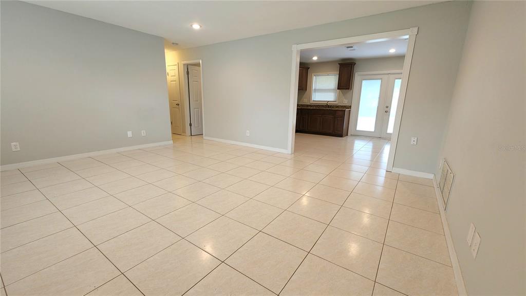 An open-concept living area features light-colored tile flooring and a doorway leading to a kitchen — 2834 STATE ROAD 590, CLEARWATER, FL