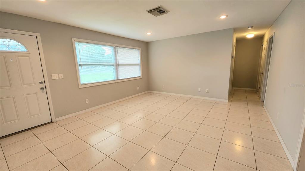 A bright, empty living room features light-colored tile flooring, gray walls, and a front door — 2834 STATE ROAD 590, CLEARWATER, FL