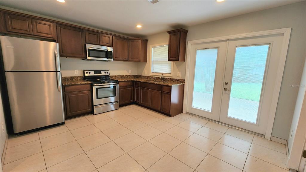 A kitchen features dark wood cabinets, granite countertops, stainless steel appliances, and light tile flooring — 2834 STATE ROAD 590, CLEARWATER, FL