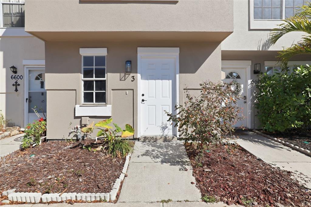 The exterior of a multi-unit residential building features white doors, a window, and landscaping — 6600 121ST AVENUE N UNIT 3, LARGO, FL