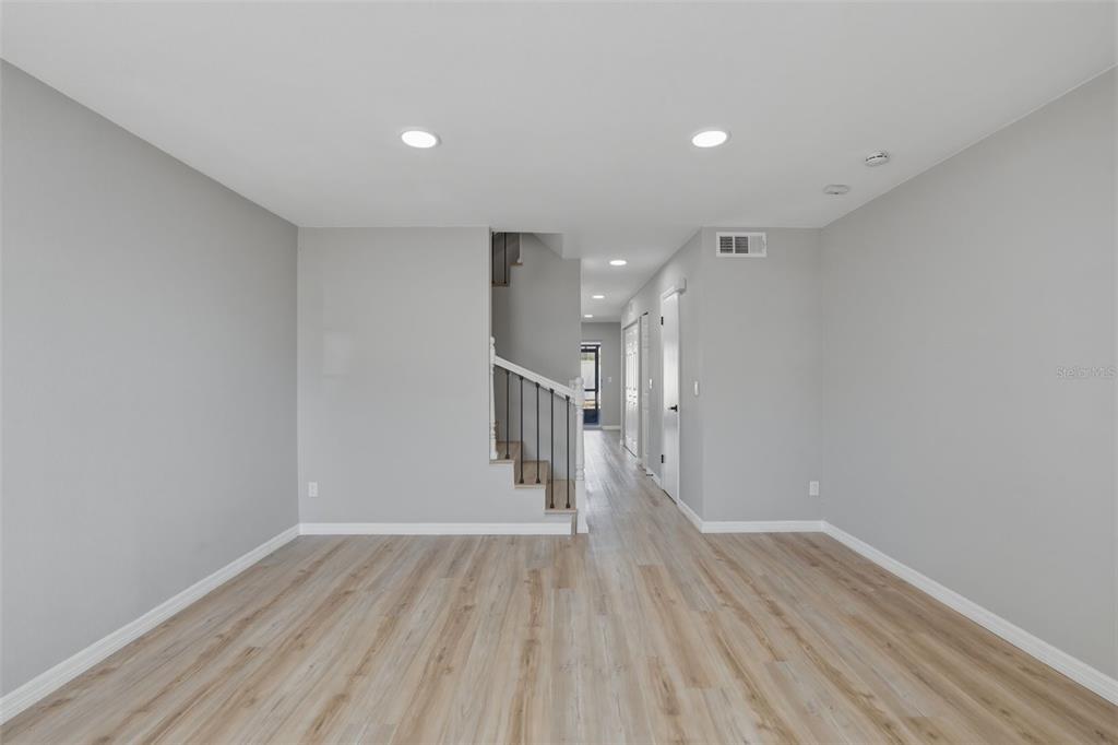 A living area features light wood-look flooring, gray walls, and a staircase with black railings — 6600 121ST AVENUE N UNIT 3, LARGO, FL