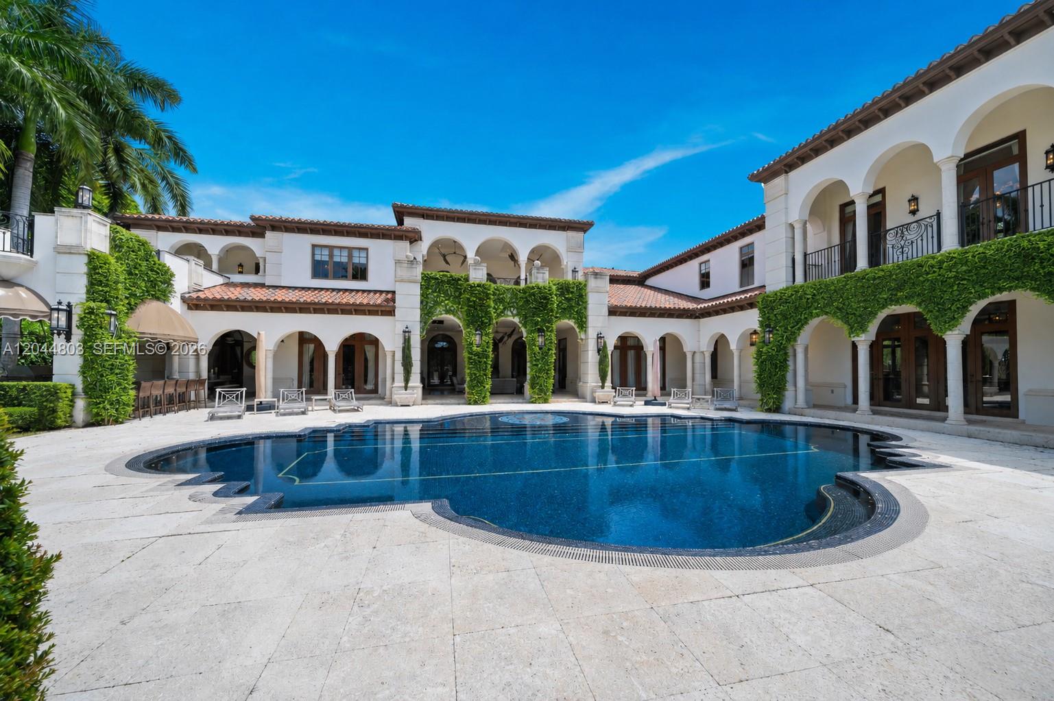 A large swimming pool sits in the courtyard of a Mediterranean-style mansion with arched walkways — 150 Edgewater Dr, Coral Gables FL 33133, CORAL GABLES, FL