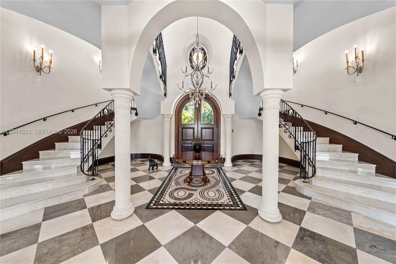 A grand foyer features a checkerboard marble floor, dual curved staircases, and a central chandelier — 150 Edgewater Dr, Coral Gables FL 33133, CORAL GABLES, FL