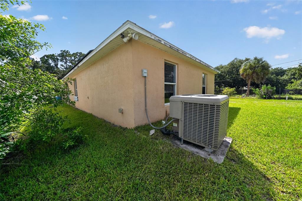 The exterior side of a tan house features an HVAC unit on a concrete pad — 1081 JOHNSTON ROAD SE, PALM BAY, FL