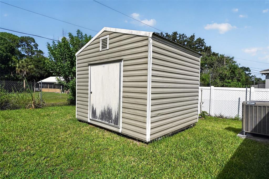 A tan metal storage shed sits in a grassy backyard near a white fence — 1081 JOHNSTON ROAD SE, PALM BAY, FL