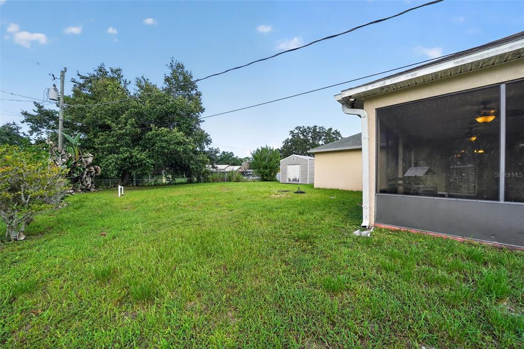 A grassy backyard features a screened-in patio, a small storage shed, and mature trees — 1081 JOHNSTON ROAD SE, PALM BAY, FL