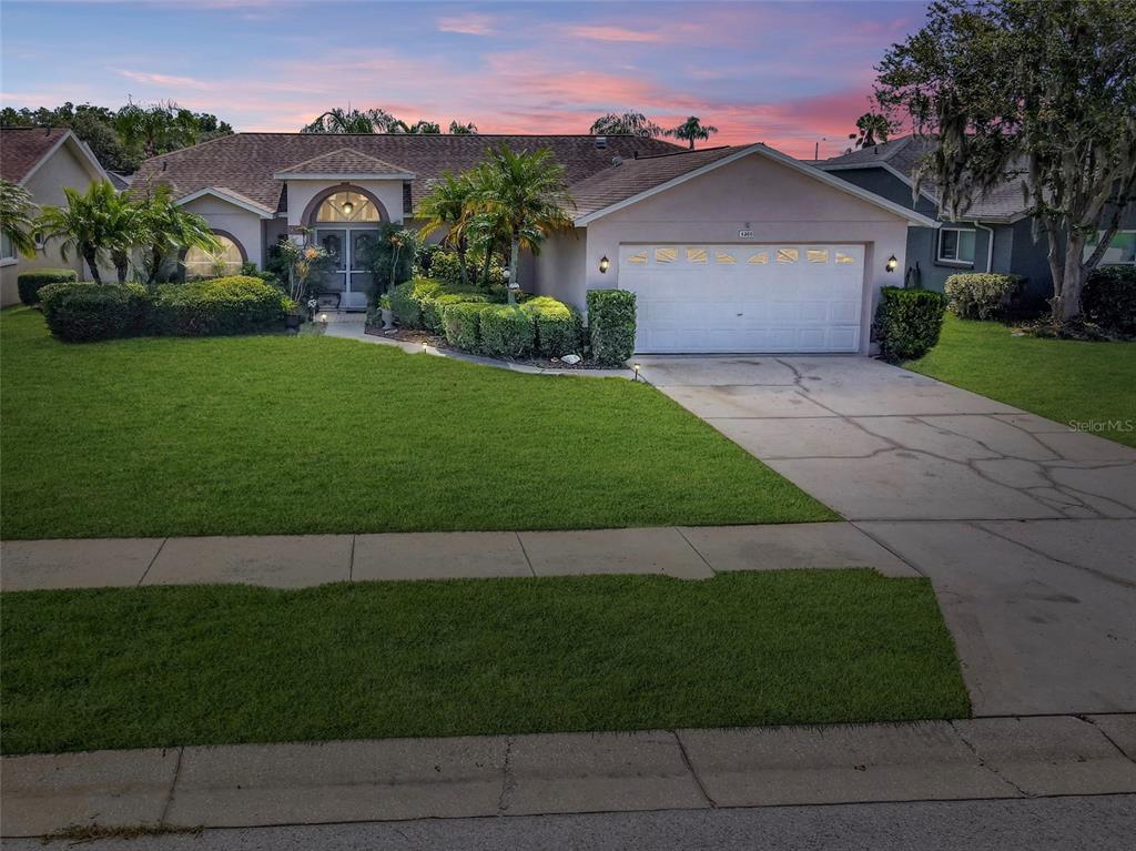 A single-story house with a two-car garage, manicured lawn, and landscaping at sunset — 4300 ONORIO STREET, NEW PORT RICHEY, FL