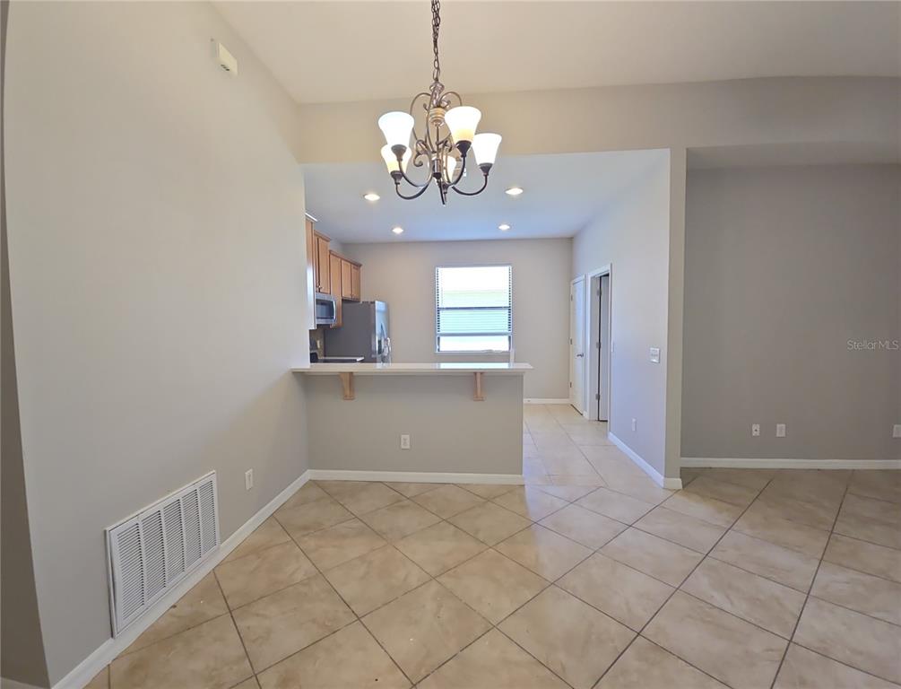 A dining area with tile floors and a chandelier opens to a kitchen with a bar — 5201 SUNSET CANYON DRIVE, KISSIMMEE, FL
