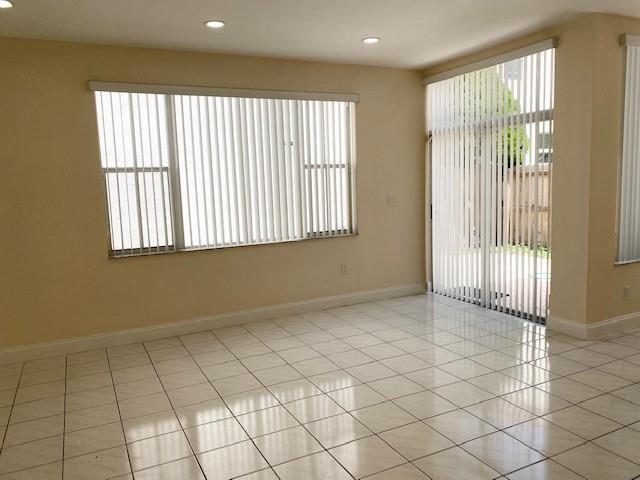 An empty room with light-colored tile flooring, vertical blinds, and a sliding glass door — 3145 N 37th Avenue, Hollywood FL 33021, HOLLYWOOD, FL