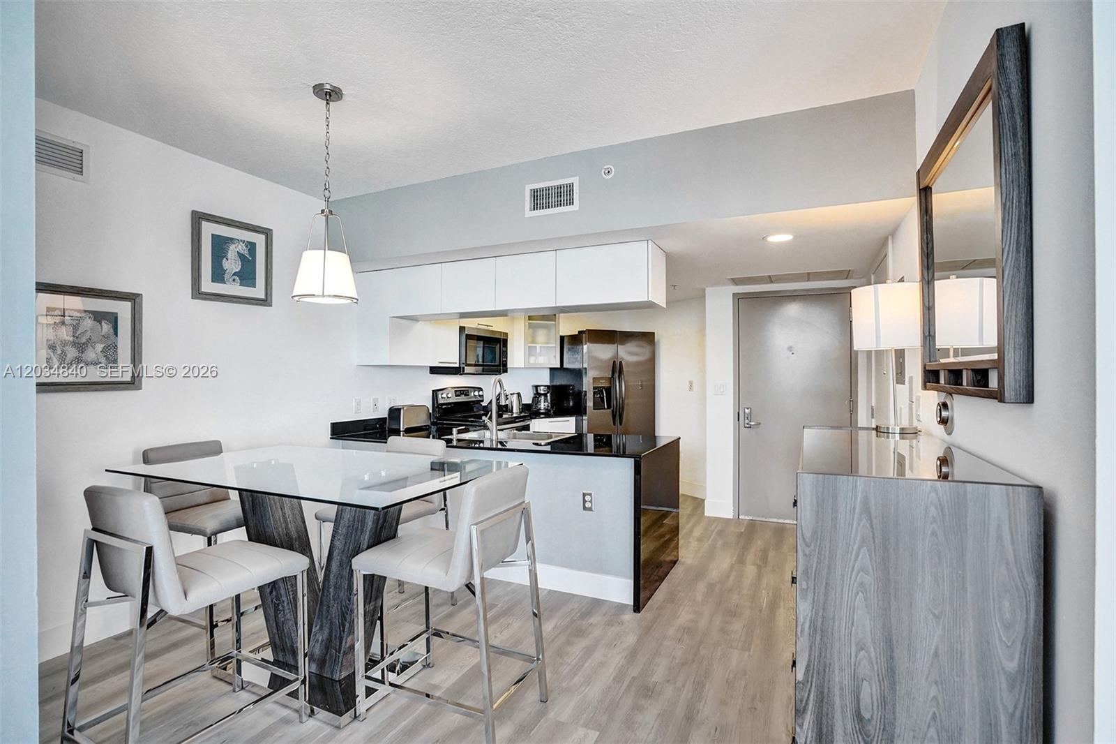 A modern kitchen and dining area feature a glass table, white cabinets, and stainless appliances — 1750 N Bayshore Dr # 3802, Miami FL 33132, MIAMI, FL