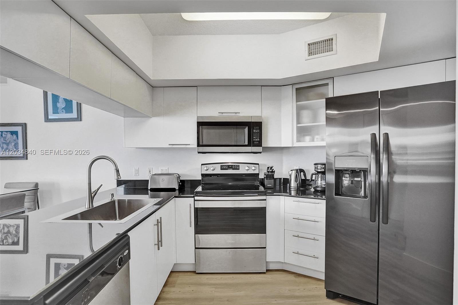 A modern kitchen features white cabinets, black countertops, and stainless steel appliances — 1750 N Bayshore Dr # 3802, Miami FL 33132, MIAMI, FL