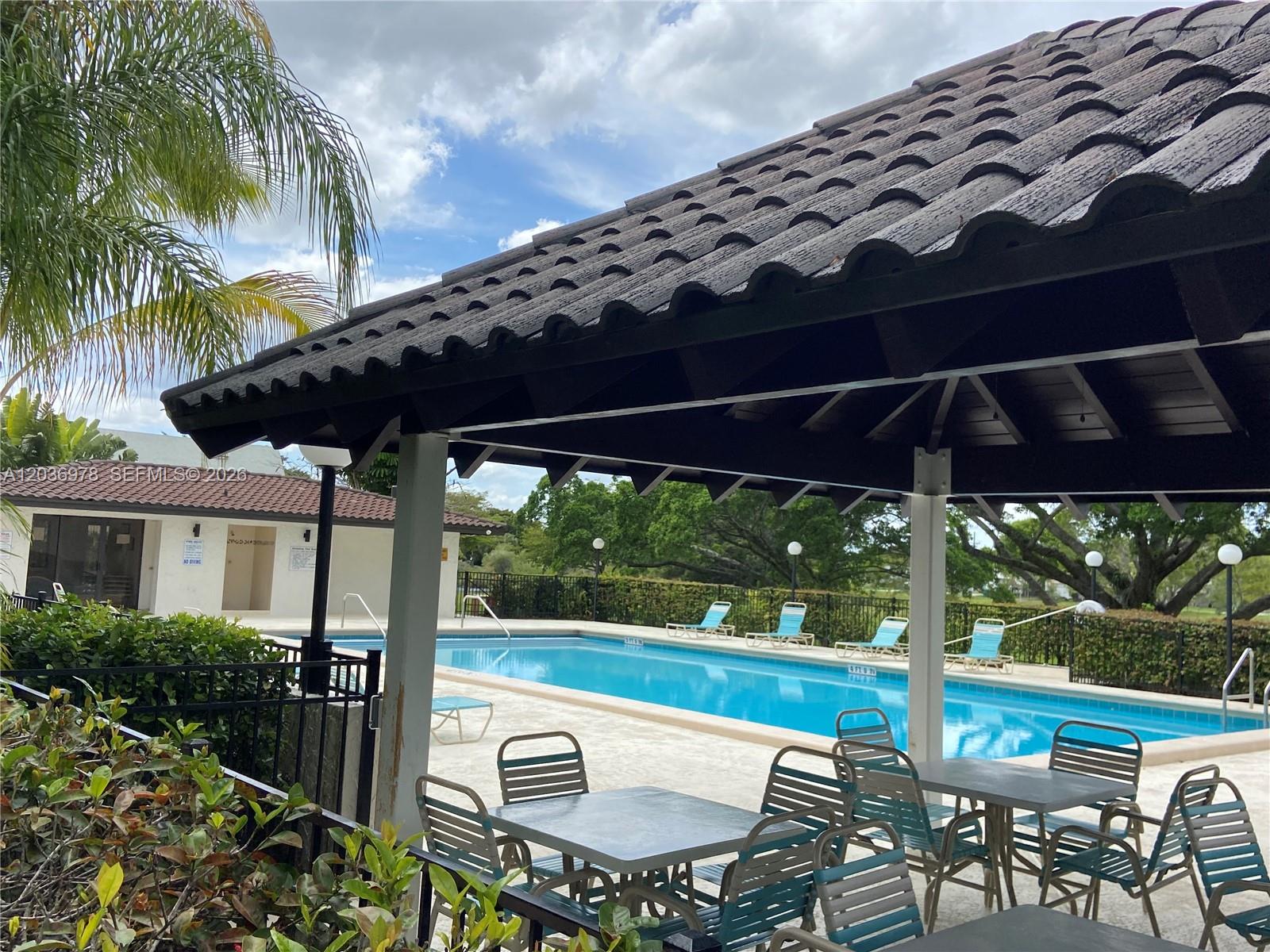 A covered patio with outdoor seating overlooks a rectangular swimming pool and a small building — MIAMI, FL