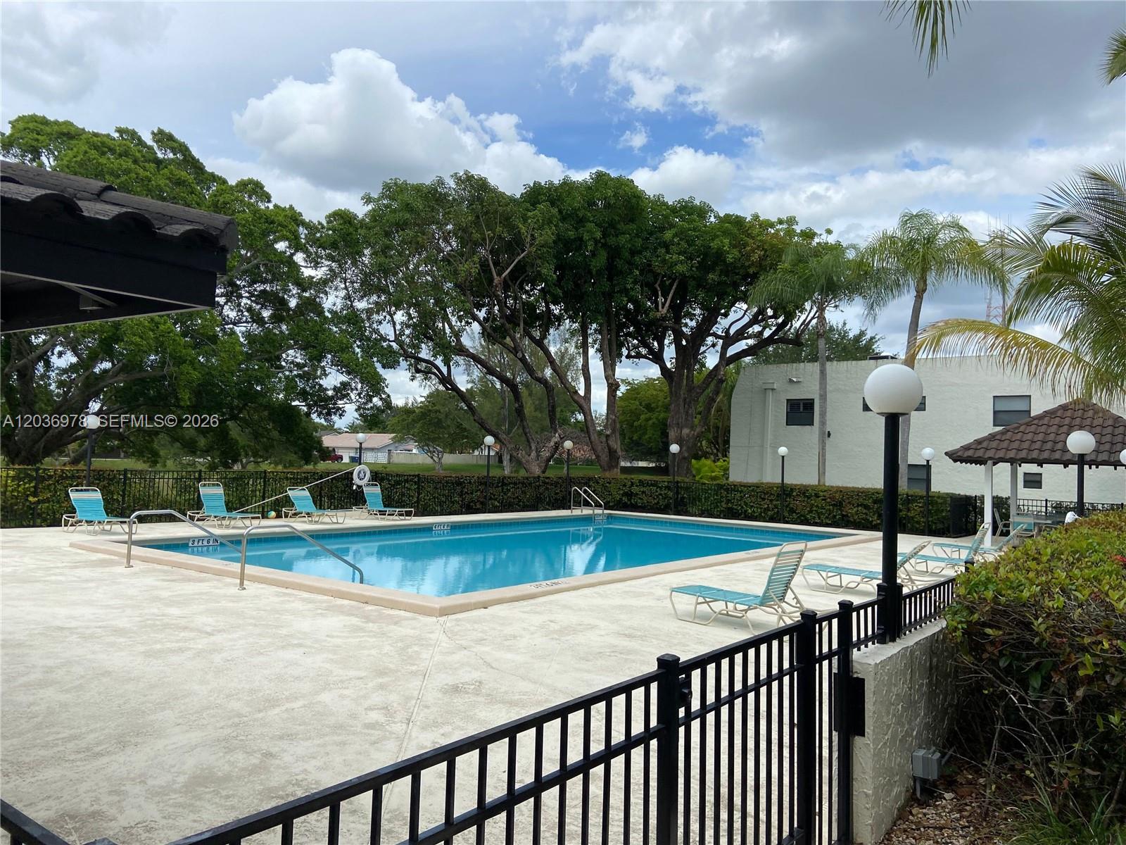 A rectangular swimming pool is surrounded by a concrete deck, lounge chairs, and mature trees — MIAMI, FL