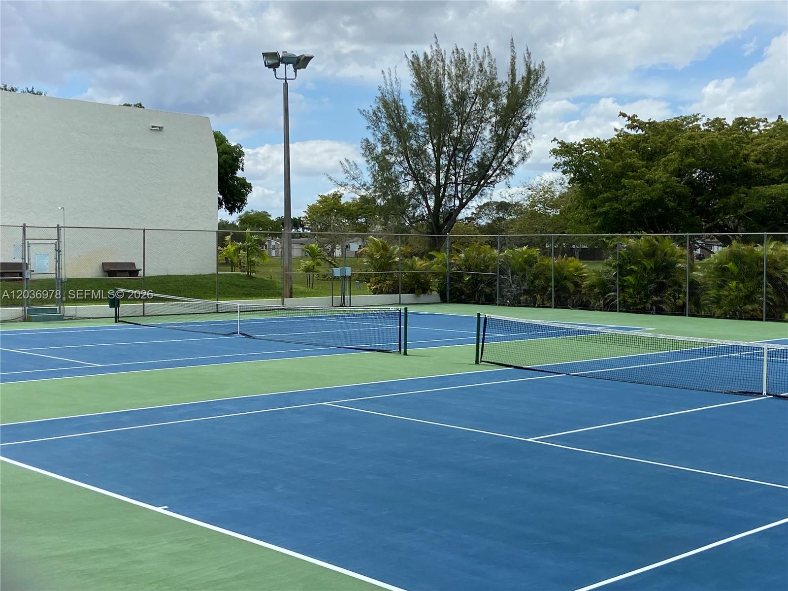 A fenced outdoor tennis court with blue and green surfaces under a cloudy sky — MIAMI, FL