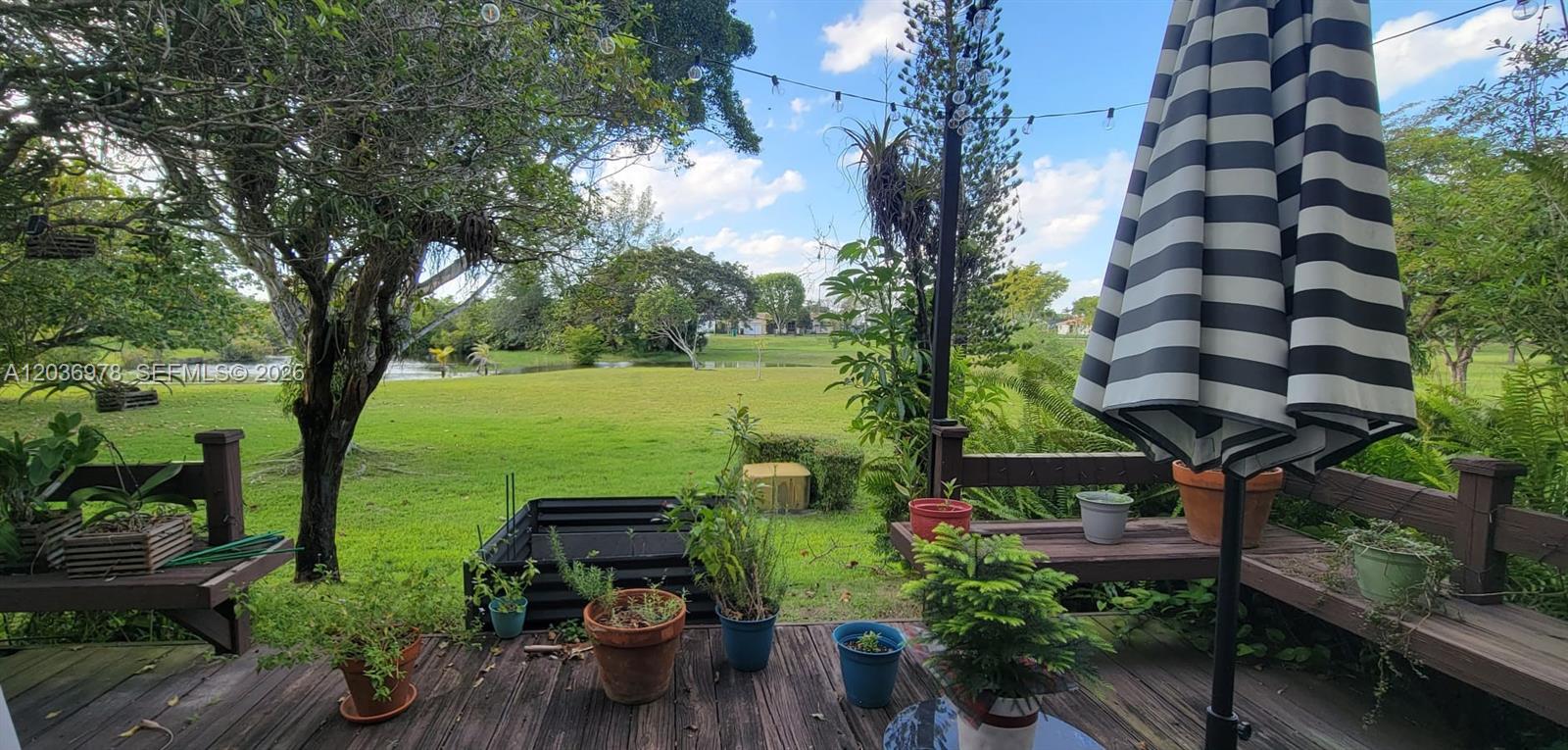 A wooden deck features potted plants, a striped umbrella, and a view of a grassy yard — MIAMI, FL