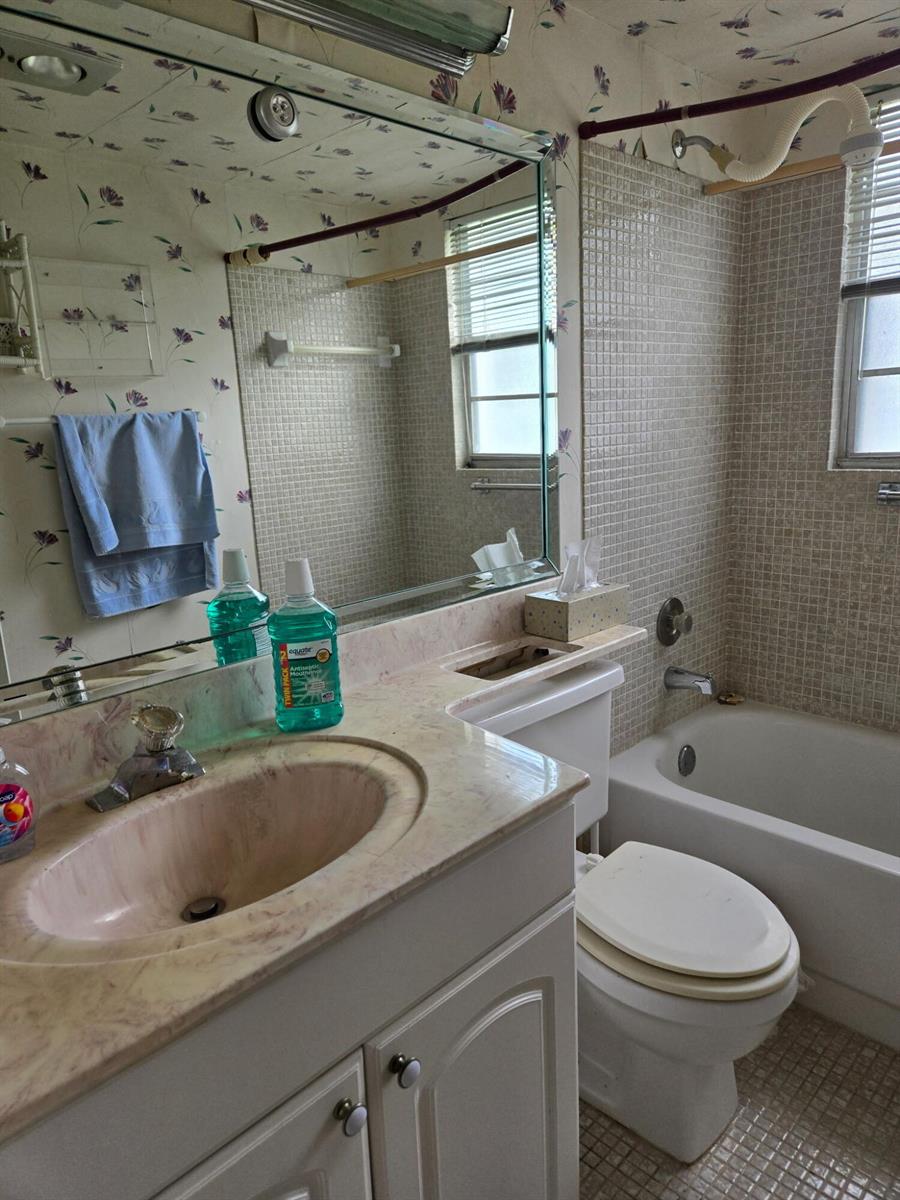 A bathroom features floral wallpaper, a vanity with a pink countertop, and a tiled tub — 177 Upminster I # 177, Deerfield Beach FL 33442, DEERFIELD BEACH, FL
