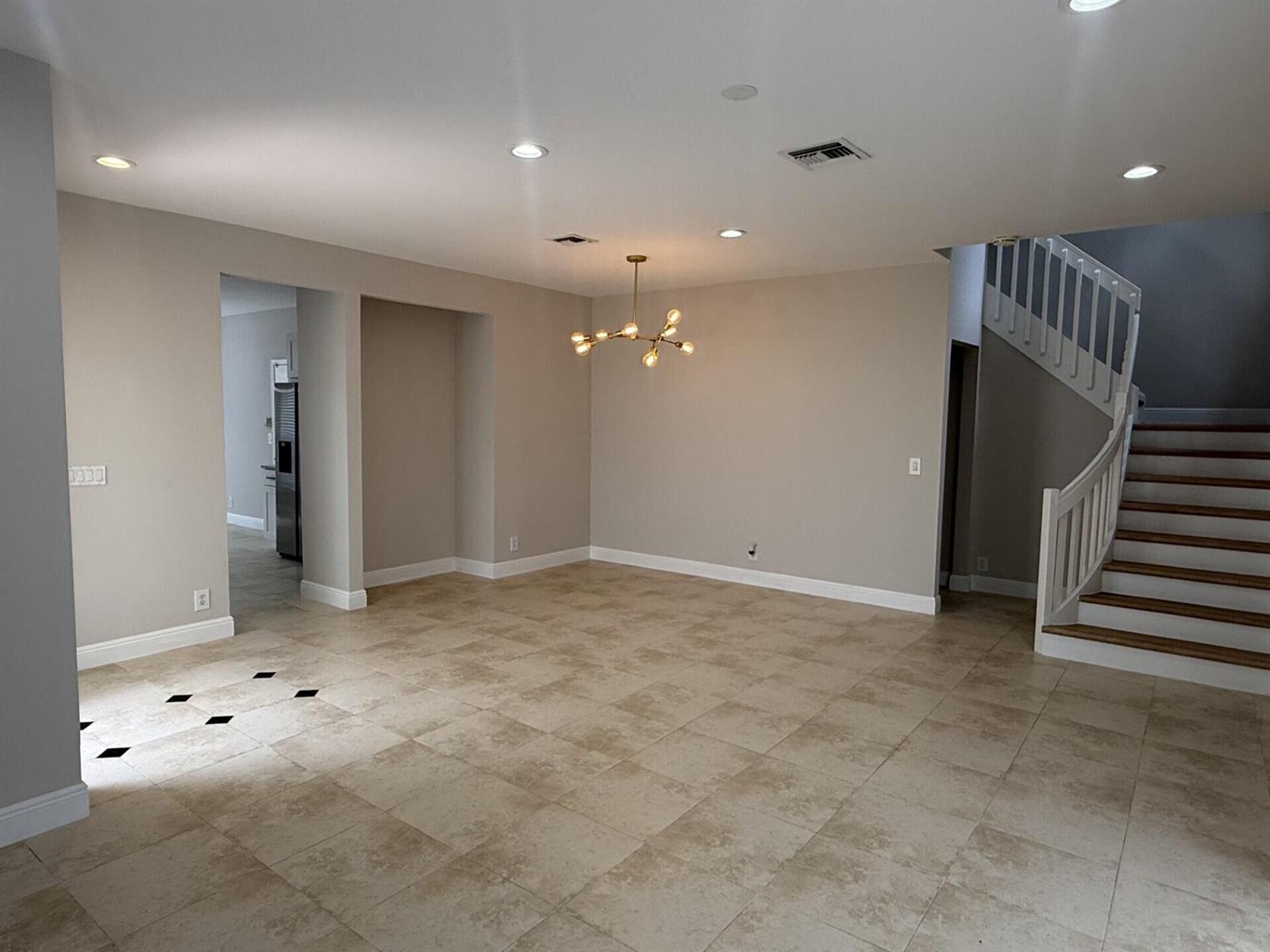 An empty dining area features beige tile flooring, a modern chandelier, and a wooden staircase — 7218 Panache Way, Boca Raton FL 33433, BOCA RATON, FL