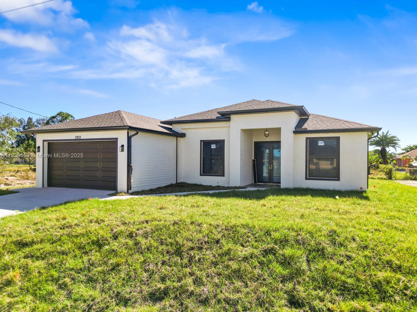 A single-story house with a white stucco exterior, dark trim, and an attached two-car garage — 2803 44TH ST SW, Lehigh Acres FL 33976, LEHIGH ACRES, FL