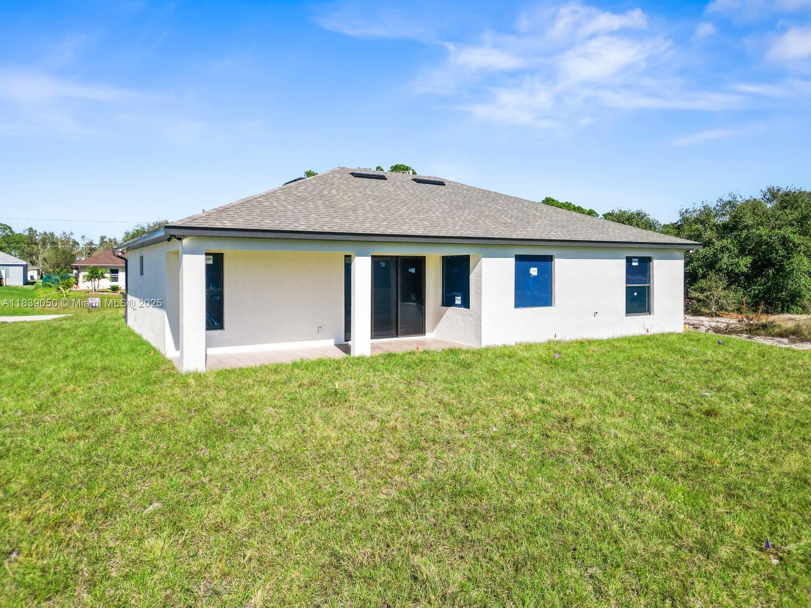The exterior rear view of a single-story house features a covered patio and lawn — 2803 44TH ST SW, Lehigh Acres FL 33976, LEHIGH ACRES, FL