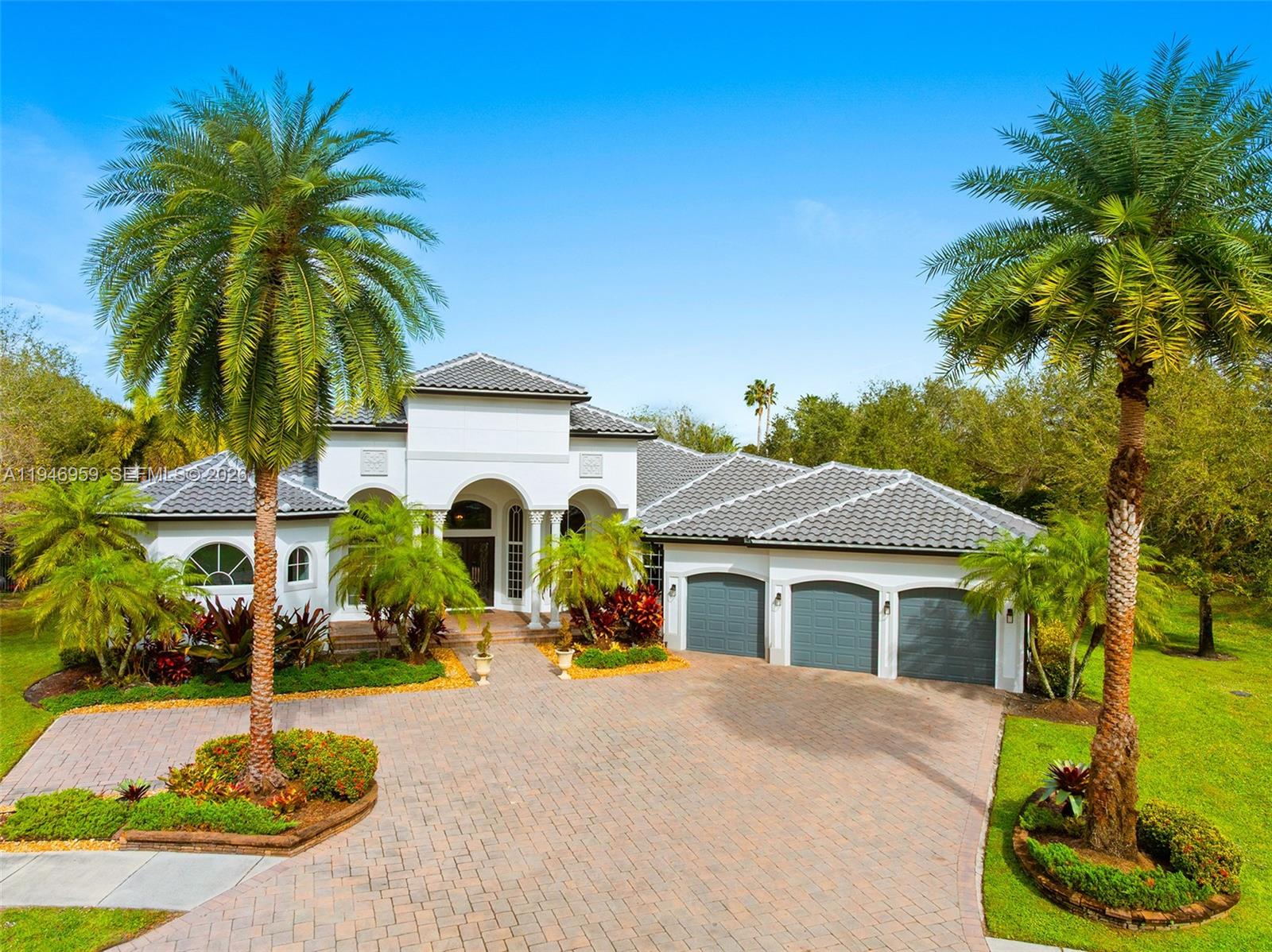 A white single-story house with a tiled roof, three-car garage, and two prominent palm trees — 12401 N Stonebrook Cir, Davie FL 33330, DAVIE, FL