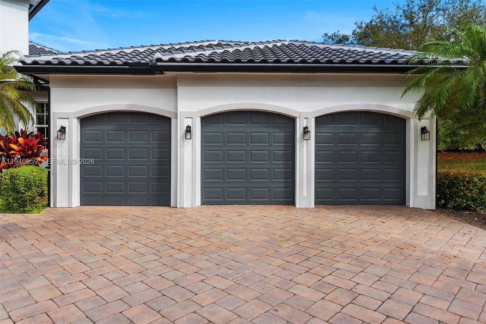 A three-car garage with dark gray paneled doors and arched stone trim under a tile roof — 12401 N Stonebrook Cir, Davie FL 33330, DAVIE, FL