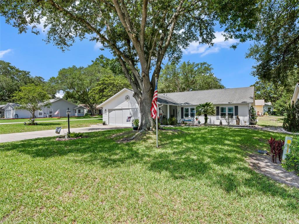 A single-story white house with a large oak tree and an American flag in front — 1622 NEW ABBEY AVENUE, LEESBURG, FL