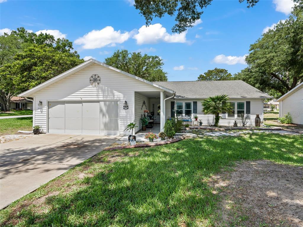 A single-story white house with a two-car garage and a front porch under trees — 1622 NEW ABBEY AVENUE, LEESBURG, FL