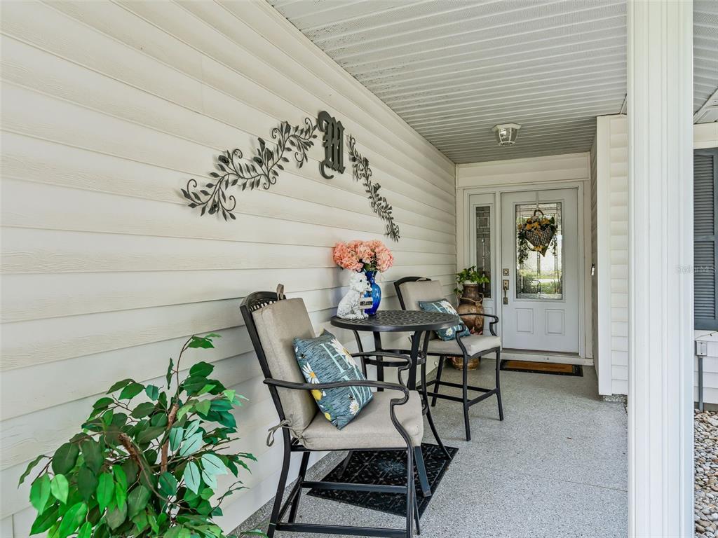 A covered front porch features a small bistro set, decorative wall art, and a front door — 1622 NEW ABBEY AVENUE, LEESBURG, FL