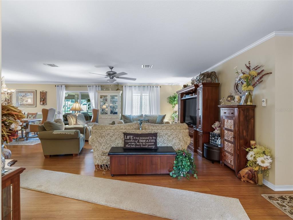 A living room features hardwood floors, a floral sofa, a wooden entertainment center, and ceiling fans — 1622 NEW ABBEY AVENUE, LEESBURG, FL